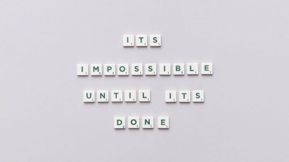 Motivational phrase 'It's impossible until it's done' arranged with Scrabble tiles on a gray background.