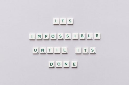 Motivational phrase 'It's impossible until it's done' arranged with Scrabble tiles on a gray background.